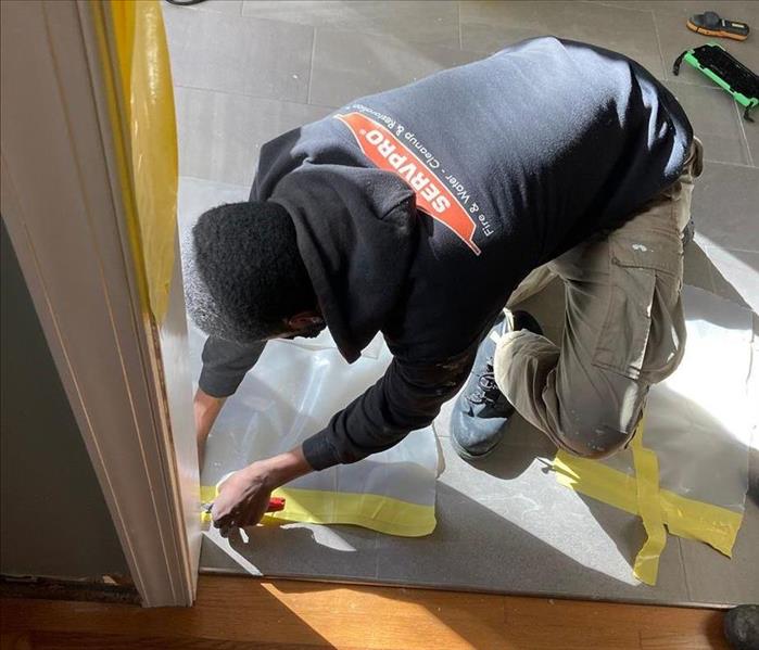 SERVPRO technician by a doorway with tape and floor covering